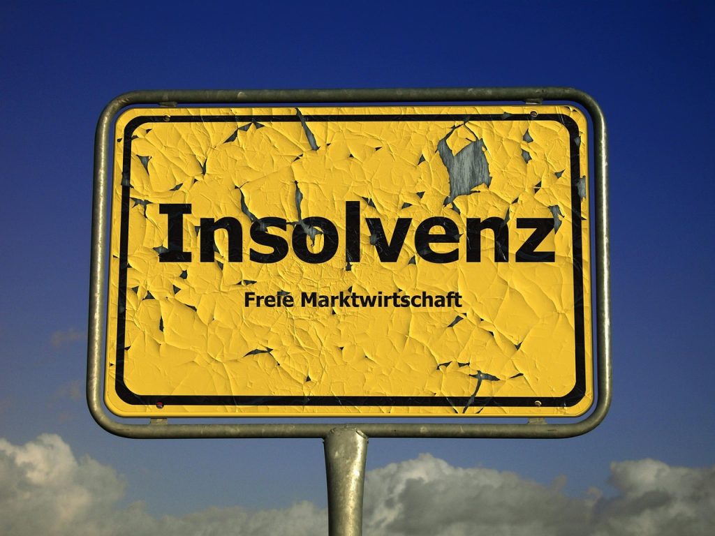 Yellow sign with cracked paint reads Insolvenz Freie Marktwirtschaft under a blue sky