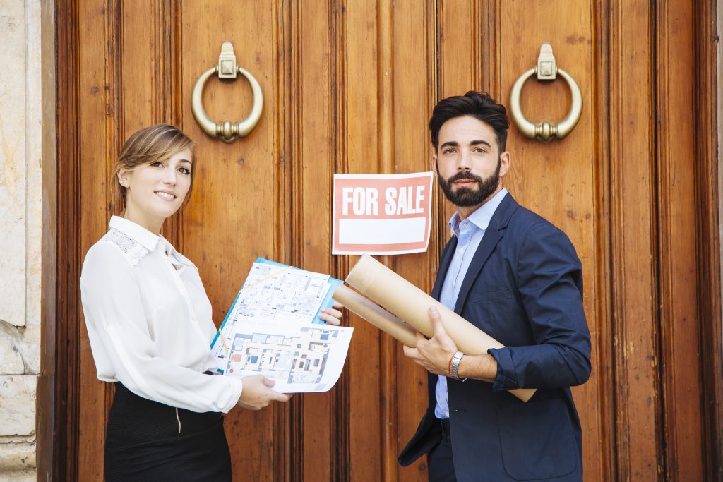Estate agents with property plans outside house for sale sign