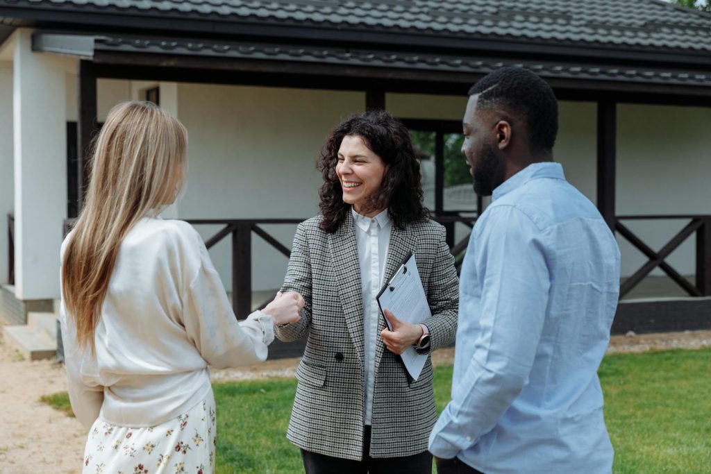 Estate agent smiling and shaking hands with clients outside a new property